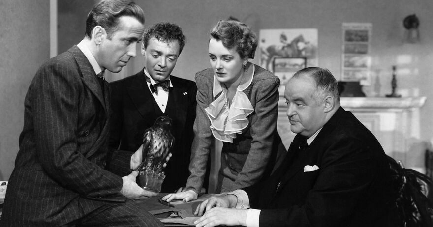 A black and white photo of four people crowded around The Maltese Falcon.