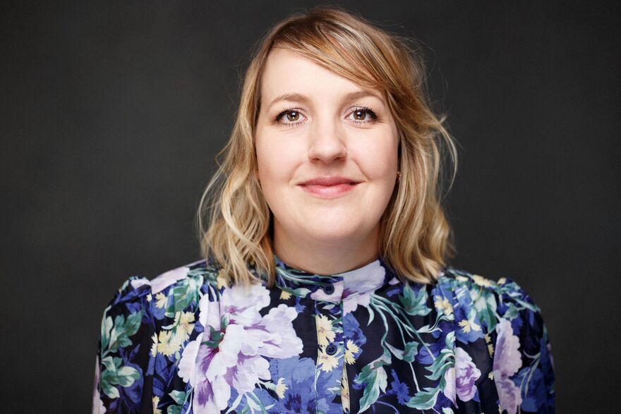 Headshot of mezzo-soprano Eleanor Minney smiling in a dark blue floral blouse.