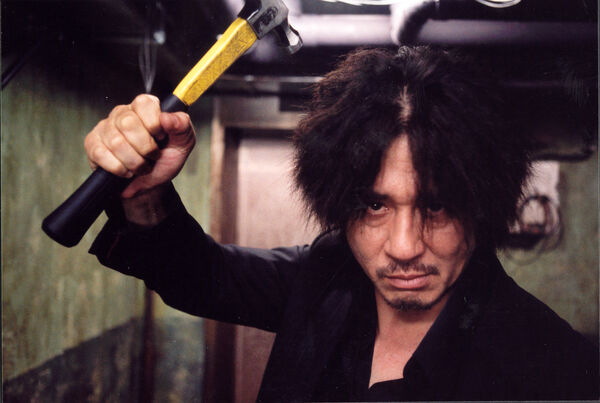 A man holds up a hammer, looking straight to camera. 