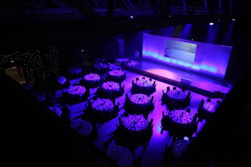 Circle tables with chairs around them in front of a stage lit in purple light