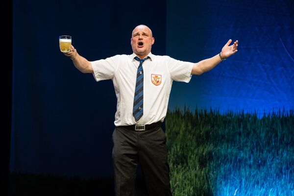 Al Murray standing on stage holding a beer up
