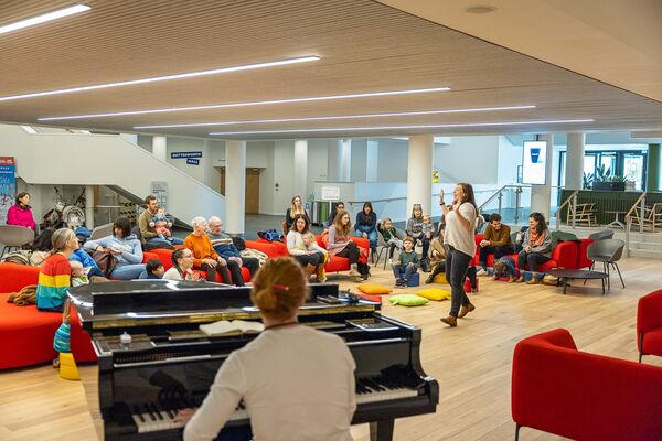 One woman sat at piano, another stood singing and families sat on sofas watching 