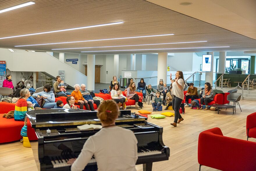 One woman sat at piano, another stood singing and families sat on sofas watching 