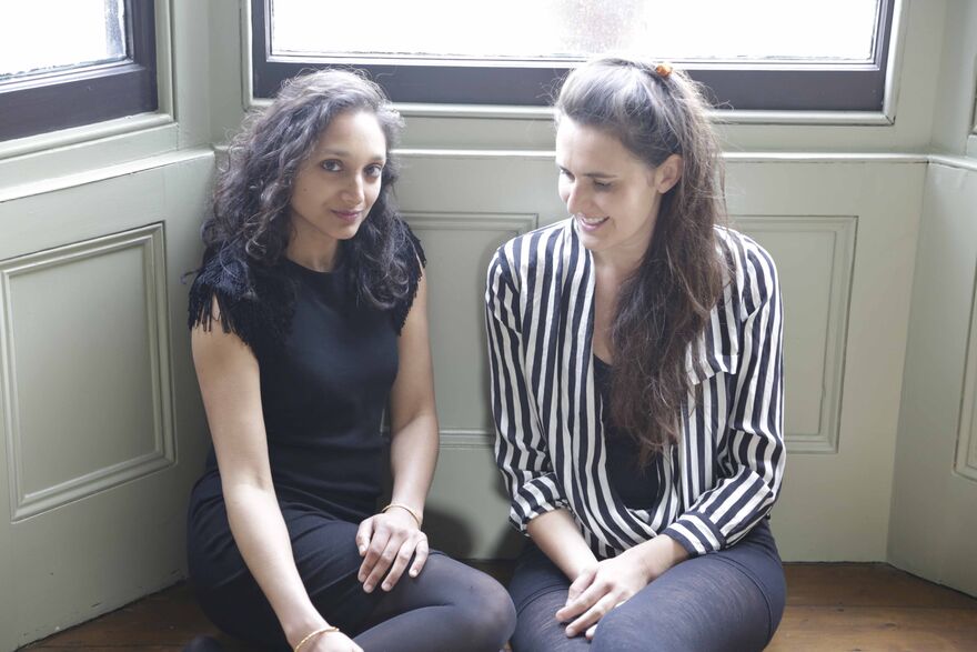 Two women dat on the floor next to a window